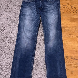 Jack & Jones blå jeans Regular Clark - Snygga blå jeans från Jack & Jones i modellen Regular Clark. Jeansen har klassisk femficksdesign, raka ben och coola slitningar framtill. Passar dig som gillar en normal passform och tidlös stil. Perfekt till sneakers eller boots. Storleken är 29w och 30L denna produkt är Andvönd bara några gånger så inga fel på den. Dessa jeans är Jack and Jones intelligence kollektion vilket är ett bättre miljö alternativ men lite dyrare köpt för 900 kr