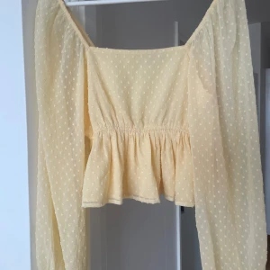 Ljusgul prickig blus från NA-KD - Superfin ljusgul blus från NA-KD med prickigt mönster och volang nedtill. Blusen har långa puffärmar med resår vid ärmslut och en söt, omlottliknande passform