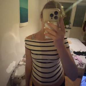 Randig offshoulder topp i bomull - Säljer en snygg offshoulder topp med breda svarta och vita ränder. Toppen har en cool båtringad hals och sitter tight mot kroppen. Perfekt för dig som gillar en fräsch och trendig look. Materialet känns mjukt och är troligen bomull.