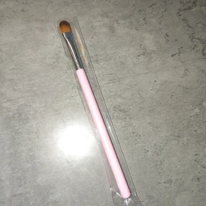 Borste - Snygg borste med ljusrosa skaft och mjuka syntetborst i brunt. Borsten har en platt och rundad form som gör det enkelt att bygga naglar men även att blenda ögonskugga. Perfekt storlek för att skapa detaljerade looks.