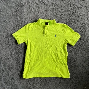 Ralph Lauren piké  - Säljer en riktigt fräsch neongrön pikétröja från Polo Ralph Lauren med klassisk krage och korta ärmar. Tröjan har blå broderad logga på bröstet och knäppning vid halsen. Perfekt för dig som vill sticka ut med färg i sommar! Längd ca 67 cm, bredd ca 47 cm. Storleken är L 14-16 år vilket bör motsvara XS men uppmärksamma måtten! PIKÉN HAR EN DEL FLÄCKAR som jag inte prövat tvätta bort men därav priset :)