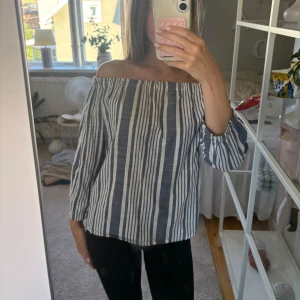 Randig offshoulder blus  - Säljer en chill randig blus med offshoulder och trekvartsärm. Toppen är vit och mörkblå med breda och smala ränder, har en luftig passform och är gjord i mjuk bomull. Perfekt för dig som gillar avslappnad stil med lite edge. Storlek 38💓