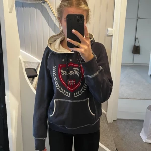 Mörkblå hoodie från Gant med tryck - Säljer en mörkblå hoodie från Gant i storlek M med stort rött och vitt tryck framtill. Tröjan är i mycket bra skick och det ända är en liten blå fläck längst fram som man kan se på 3e bilden.
