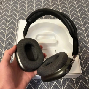 AirPod Max Svart (Med kvitto) - Bilderna visar ett par vita over-ear hörlurar med modern design och mjuka öronkuddar. Produkten levereras med ett skyddsfodral och originalförpackning. Perfekt för dig som älskar musik och vill ha stilrena hörlurar med hög komfort. Skriv om kvitto!