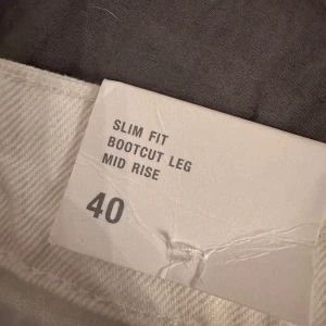 Vita bootcut byxor med snörning - Snygga vita byxor med bootcut-ben och slim fit passform. De har en cool snörning framtill istället för vanlig dragkedja, vilket ger en unik look. Byxorna är midwaist och gjorda i ett mjukt bomullsmaterial som känns skönt mot huden. Perfekta för dig som vill sticka ut lite extra.