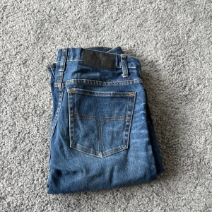 Blå jeans tiger of Sweden 30/34 - Snygga blå jeans från tiger of Sweden , modell blaise, i storlek 30/34. Klassisk femficksdesign med kontrastsömmar och rak passform. Jeansen har en mörkblå ton med lätt slitning på låren och är tillverkade i slitstarkt denimtyg. Perfekt för dig som gillar en enkel och stilren look.