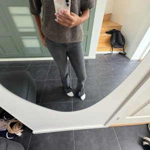 Grå bootcut jeans med mid waist - Säljer ett par grå jeans med bootcut passform och mid waist. Jeansen har klassiska fem fickor, dragkedja, knapp framtill och öppen slits ner till. Materialet är stretchigt denim som sitter snyggt och bekvämt. Perfekt för dig som gillar en tidlös och chill look.