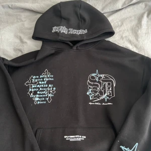Svart hoodie från Supply & Demand - Säljer en svart hoodie från Supply & Demand med tryck i vitt och blått framtill samt text på huvan. Hoodien har känguruficka och coola grafiska detaljer. Perfekt för dig som gillar streetwear. Helt nytt skick. Pris går och förhandlas.