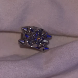 Silvrig ring med nitar - Edblad silvrig ring med upphöjda nitar i ett geometriskt mönster. Ringen har en bred design och ger en edgy känsla till din stil. Perfekt för dig som gillar statement-smycken💓Nyskick 