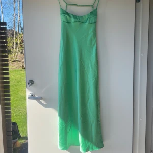 Grön långklänning i satin från Zara - Säljer en ljusgrön långklänning från Zara i glansigt satinmaterial. Klänningen har smala axelband och en elegant, enkel design med lätt utställd passform. Perfekt för sommarens tillfällen när du vill sticka ut med färg. Den har några märken, men inget som man tänker på om man inte kollar på nära håll.