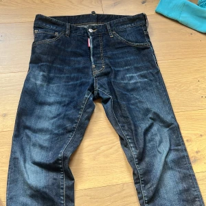 Mörkblå jeans från Dsquared2  - Säljer ett par snygga mörkblå jeans från Dsquared2, modell. Jeansen har klassisk femficksdesign, orange kontrastsömmar och en liten röd Dsquared2-tag vid fickan. Perfekta för dig som gillar en modern och stilren look.