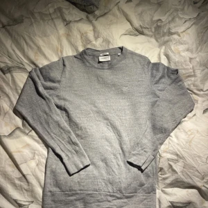 Grå merinoulltröja från Lindbergh - Säljer en stilren grå tröja från Lindbergh i mjuk merinoull. Klassisk rund halsringning och lång ärm, perfekt för lager-på-lager eller som den är. Enkel och tidlös design som passar till mycket.