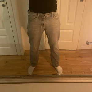 Jack & Jones jeans  - Säljer ett par grå jeans med lite relaxed/baggy passform och klassiska fem fickor. Jeansen har normal midja och stängs med knapp. Perfekta för en avslappnad stil och passar till det mesta. 