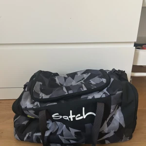 Svart och grå sportbag/weekendbag från Satch - Säljer en sportig och rymlig svart och grå axelväska från Satch med geometriskt mönster. Väskan har dragkedja, dubbla handtag och flera fack för smart förvaring. Perfekt för gymmet eller träning. Använd ca 2 ggr, pris går att diskutera🩷🩷