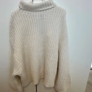 Vit stickad polotröja - Mysig och oversized vit stickad polotröja med grovstickat mönster. Tröjan har långa ärmar och en hög polokrage som ger extra värme. Perfekt för kyliga dagar och enkel att styla till olika outfits.