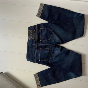 Lågmidjade jeans med detaljer - Mörkblåa jeans från MET, köpta second hand i nyskick. Tänkte klippa till shorts men de passade tyvärr inte mig. De är slim i modellen men hade varit riktigt snygga som shorts eller omsydda till bootcut. Fina stendetaljer på fickorna och lappen samt längst ner på benen. Står att de är made in Italy (sista bilden). Skriv för mått eller fler bilder!! 💗💗