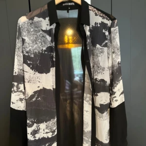 Svartvit mönstrad skjorta från Black & White - Säljer en svartvit skjorta med abstrakt mönster från Black & White. Skjortan har svarta detaljer på krage och ärmslut samt långa ärmar. Perfekt för dig som vill sticka ut med en unik stil.