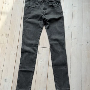 Grå Replay Anbass jeans - Snygga grå jeans från Replay, modell Anbass. Storleken är W30 och L32. Klassisk femficksdesign med dragkedja på ena bakfickan och raka ben. Jeansen har normal passform och är tillverkade i ett mjukt denimtyg.