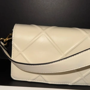 Beige/krämvit axelväska från Primark - Säljer en stilren beige/krämvit axelväska från Primark med bred axelrem. Väskan har guldfärgade metalldetaljer och stängs med magnetlås. Perfekt för att lyfta din outfit! Knappt använd. Kom gärna med bud!