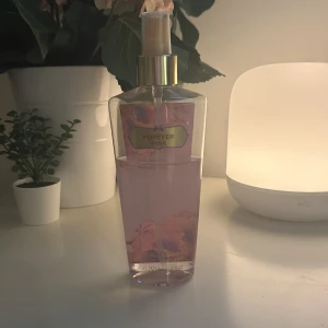 Forever Pink Body Mist från Victoria's Secret - En söt body mist i doften Forever Pink från Victoria's Secret. Flaskan är genomskinlig med rosa vätska och har en guldig spraykork. Dekorerad med blommotiv och etikett i rosa och guld. Perfekt för dig som gillar fräscha och blommiga dofter.