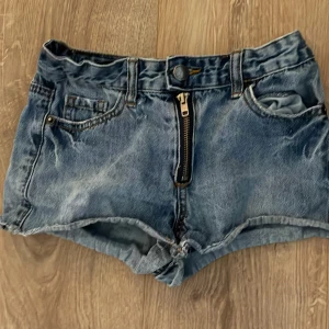 Blå jeansshorts från Union Denim - Säljer ett par klassiska blå jeansshorts från Union Denim. De har normal passform, hög midja och en tydlig dragkedja framtill. Shortsen har fem fickor och bälteshällor, samt råa kanter nedtill för en avslappnad look.