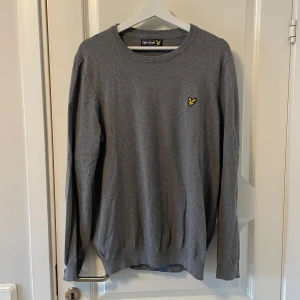 Grå tröja från Lyle & Scott - Säljer en stilren grå tröja från Lyle & Scott med rund halsringning och den klassiska gula loggan broderad på bröstet. Tröjan har långa ärmar och är perfekt för en enkel och snygg look. Storlek XL men sitter som en L