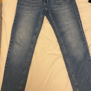 Blå raka jeans - Säljer ett par klassiska blå jeans med rak passform. Jeansen har normal midja och är tillverkade i denim. Perfekta för en avslappnad stil och passar till det mesta i garderoben.
