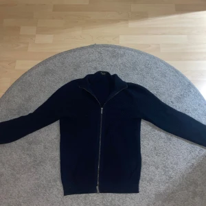 Mörkblå stickad kofta från Massimo Dutti - Säljer en mörkblå stickad kofta från Massimo Dutti med dragkedja framtill. Koftan har lång ärm och ett diskret strukturerat mönster i materialet. Perfekt för en uppklädd och vardaglig outfit.💸💸