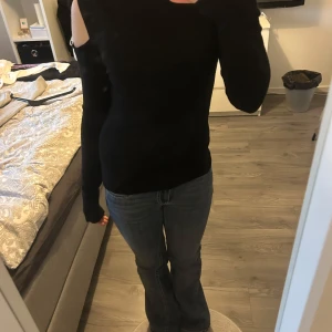 Svart långärmad topp med cut out-detalj - Säljer en svart långärmad topp med cut out-detalj på axlarna. Snygg och stilren modell som passar perfekt till jeans eller kjol. Mjuk och stretchig i materialet för en bekväm passform.