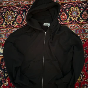 Weekday boxy zip hoodie - Säljer en svart hoodie från Weekday med dragkedja framtill och huva. Tröjan har två fickor och ribbade muddar vid ärmslut och nederkant. Perfekt för en avslappnad stil. Boxy fit. 
