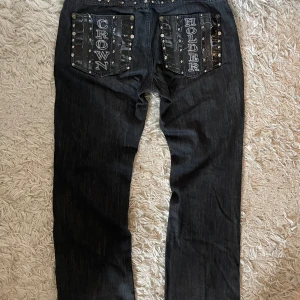 RARE Baggy y2k Crown Holder Jeans  - Säljer ett par svarta jeansbyxor från Crown Holder med unika broderade bakfickor och nitar längs fickkanterna. Byxorna har raka ben och coola detaljer både fram och bak. Perfekt för dig som vill sticka ut med din stil. 