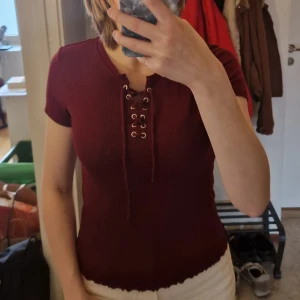 Vinröd ribbad topp med snörning från New Yorker - Säljer en vinröd ribbad topp från New Yorker storlek XS. Toppen har korta ärmar och snygg snörningsdetalj framtill. Har länge varit en favorit men säljer nu pga att den blivit lite för liten. Skriv vid frågor!✨️ Samfraktar gärna så kika in mina andra inlägg!✨️