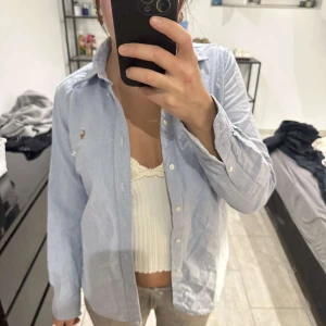 Ljusblå skjorta från Ralph Lauren - Säljer en klassisk ljusblå skjorta från Ralph Lauren med button-down krage och broderad logga på bröstet. Skjortan har långa ärmar och stängs med vita knappar framtill. Perfekt för en stilren look.