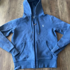 Blå hoodie från Polo Ralph Lauren - Blå zip hoodie från Polo Ralph Lauren i storlek XS, det finns två slitningar på tröjan men som inte märks av vid användning, köpt för 2199 kr