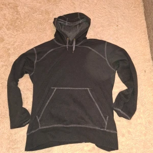 Svart hoodie från Mac One - Säljer en svart hoodie från Mac One i storlek XL men jag skulle säga att den även passar M och L. Tröjan har huva med dragsko, långa ärmar och en stor magficka framtill. Snygga kontrastsömmar i grått ger en cool detalj till den annars enkla designen.