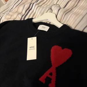 Svart stickad tröja från Ami - Säljer en svart stickad tröja från Ami med ett rött hjärta och bokstaven A broderat på bröstet. Tröjan har rund halsringning och långa ärmar. Pris går att diskutera så det är bara att skriva