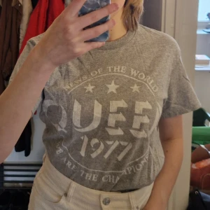 Grå Queen t-shirt med tryck - Säljer en grå Queen t-shirt med text från albumet news of the World. I storlek S och bomull. Perfekt för dig som älskar bandtröjor och Queen! Skriv vid frågor!✨️ Samfraktar gärna så kika in mina andra inlägg!✨️