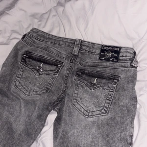 Grå jeans från True Religion - Snygga grå jeans från True Religion med låg midja och flare-stil. De har dekorativa fickor med knappar och en klassisk femficksdesign. Perfekta för en avslappnad look. Kostar runt 1000-1400 i butik men säljer för ändast 500 kr💕.(lånade bilder)
