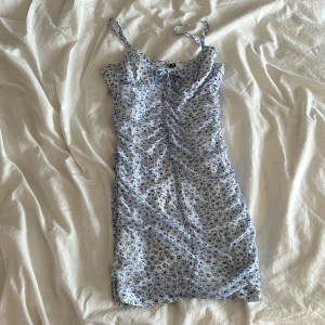 Blommig sommarklänning från H&M Divided - Söt ljusblå och vit kortklänning med små blommor från H&M Divided. Klänningen har smala axelband och en figurnära passform, perfekt för varma dagar. Tunt och lätt material som känns luftigt.