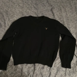 Svart v-ringad tröja från GANT - Klassisk svart v-ringad tröja från GANT med diskret logga broderad på bröstet. Tröjan har långa ärmar och ribbade muddar vid ärmslut och nederkant. Bra skick dessutom! Priset är ej hugget i sten!!