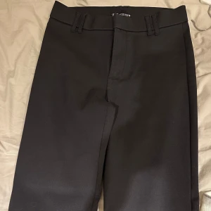 Svarta kostymbyxor med bootcut - Snygga svarta kostymbyxor med bootcut-stil. Byxorna har en högmidjad design och är perfekta för en stilren look. De har några lösa trådar vid benen. Skulle säga att de passar någon som är 160-165