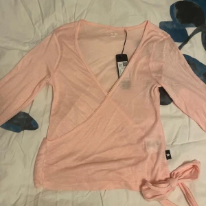Ljusrosa omlottopp - Säljer en jättefin omlottopp, i rosa. Den är ny med prislappen kvar, och helt oanvänd. Säljer pågrund av fel storlek. Den är långärmad och har knytning i sidan. Jätteskönt material. Därför är den perfekt för både vardag, pilates och finare tillfällen. Priskan diskuteras, de är bara skriva till mig.🥰