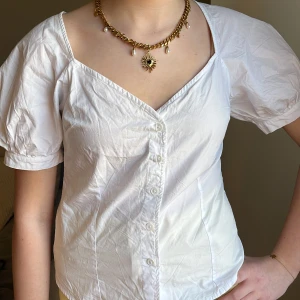 Vit blus med puffärmar och knappar - Säljer en söt vit blus med puffiga kortärmar och v-ringning. Blusen har inga defekter. 