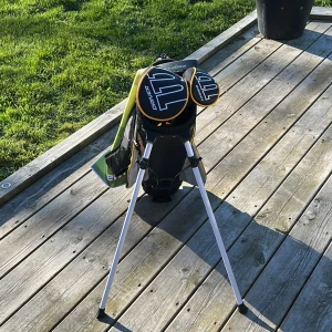 Svart och gul golfbag med stativ - Jag säljer en svart och gul golfbag med många fack och axelremmar. Den är även snygg och ha räven en sportig design. Den är för 9-11år och har en driver, hybrid, wedge, short iron och en putter. Men den kommer även med en höger handske, några peggar och 10 stycken helt nya och rena bollar;) Det går även att förhandla pris och fråga gärna frågor!