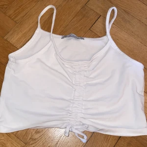 Vit croppad linnetopp från Terranova - Säljer en vit croppad linnetopp från Terranova med smala axelband och snygg rynkdetalj framtill med knyt längst ner. Perfekt för varma dagar och enkel att matcha med jeans eller kjol.