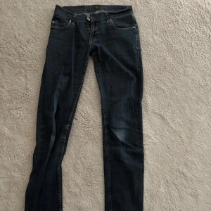 Mörkblå jeans från Tiger of Sweden - Säljer ett par mörkblå jeans från Tiger of Sweden, modell Blaise. Jeansen har klassisk femficksdesign, raka ben och normal passform. Snygga detaljer med silverfärgade nitar och knapp. Perfekta till många olika outfits.