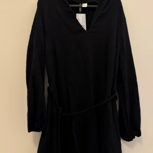 Svart blus med knyte från H&M - Svart blus från H&M med v-ringning och knytskärp i midjan. Klänningen har en enkel och stilren design, perfekt för dig som gillar minimalistiskt mode. Aldrig använd, prislappen kvar. Kan gå ner i pris vid snabb affär!💕