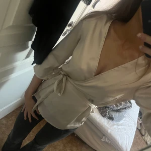 Beige omlottblus med knytband - Säljer en stilren beige omlottblus med knytband i midjan. Blusen har trekvartsärm och djup v-ringning🩷