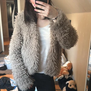 Beige teddyjacka med fluffig look - Säljer en supermjuk och fluffig beige teddyjacka med lång ärm. Jackan har en oversized passform och är perfekt för dig som vill ha en mysig och trendig stil. Passar till många olika outfits och håller dig varm under kyliga dagar.