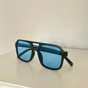 Svarta solglasögon med blåtonade glas - Snygga solglasögon med svart båge och rektangulär form. Glasen är blåtonade och ger en cool retrovibe🤵🏼Perfekta för att sticka ut i sommar☀️Bågarna är i plast och modellen är oversized😎
